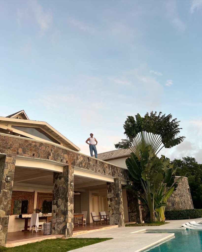 Taika stands, hand on hips, looking out at the view from the second floor of their Caribbean villa.