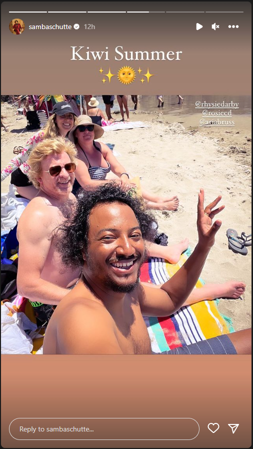 Samba takes a selfie with Rhys and both of their partners, sitting on the sandy beach.