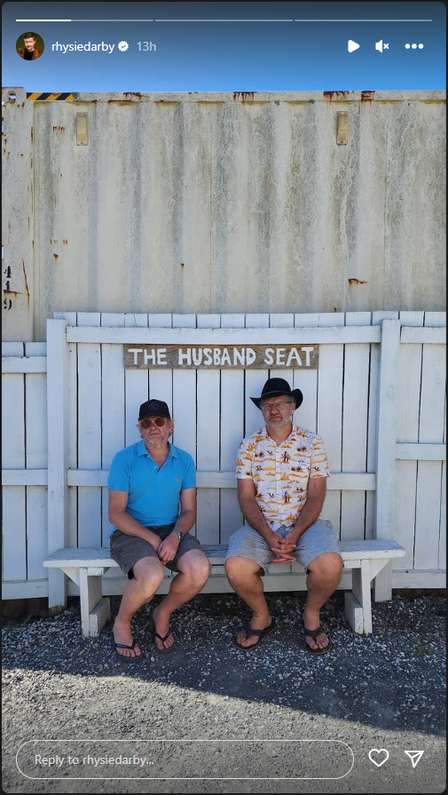 Rhys and Buttons sit on a white bench. Painted sign above them reads: "The husband seat."