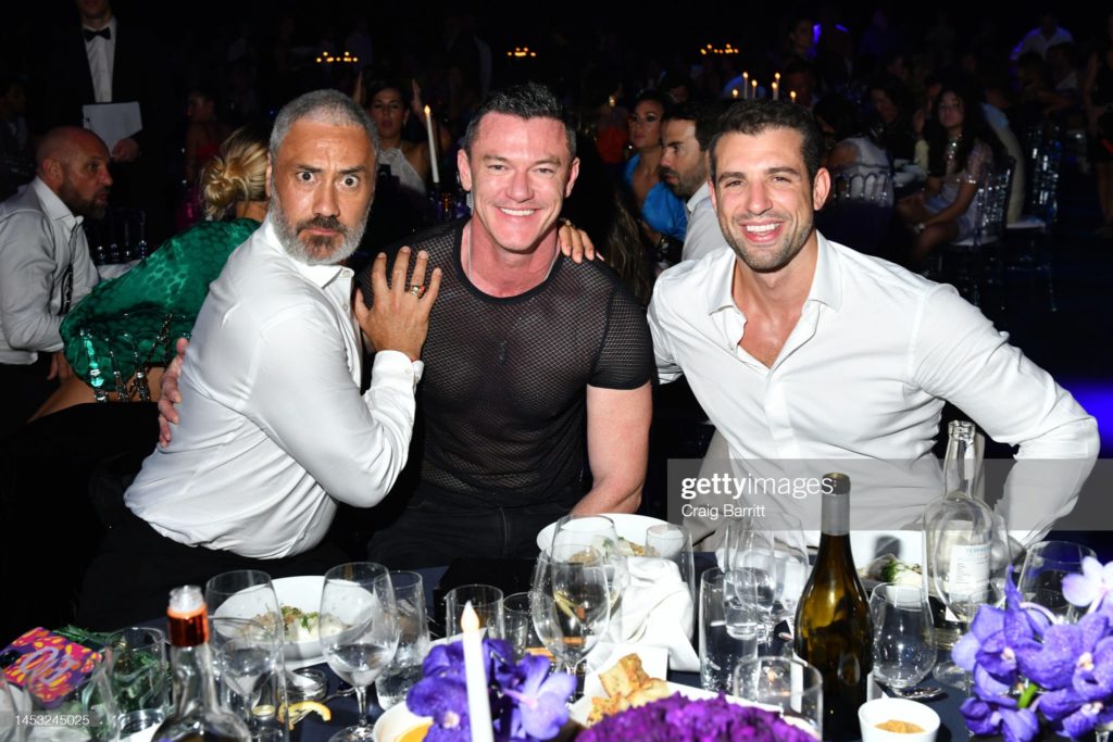 Taika Waititi poses with wide eyes and a raised eyebrow, hand on Luke Evans' shoulder. Tommaso Chiabra is also there.