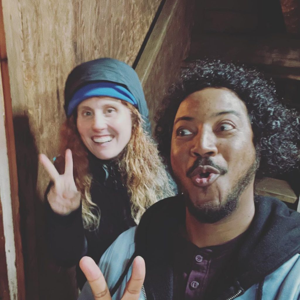 Samba and a female-presenting cast or crew member make peace signs as Samba takes a silly selfie.