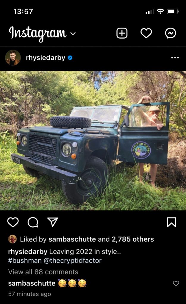Rhys stands behind, and arm draped over, the open door of a Jeep that has the Cryptid Factor logo on it. Rhys appears to have no clothes on (except a safari hat). Text says: "Leaving 2022 in style... #bushman"