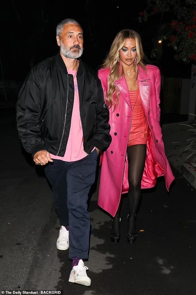 Rita wears a Barbie pink dress and leather jacket. Taika matches her with a light pink shirt and black bomber jacket.
