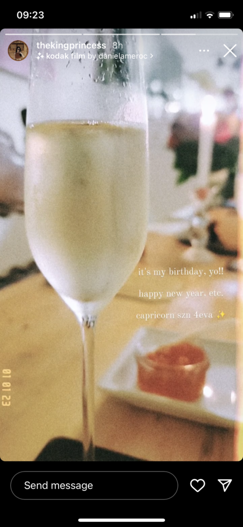 A close-up of a champagne flute, a restaurant table blurry in the background. Text reads: "It's my birthday, yo! Happy new year, etc. Capricorn szn 4eva"