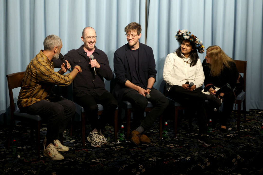 Taika holds a mic in his hand, sitting next to and laughing with a panel of four other people, the creators of the film "The Territory."