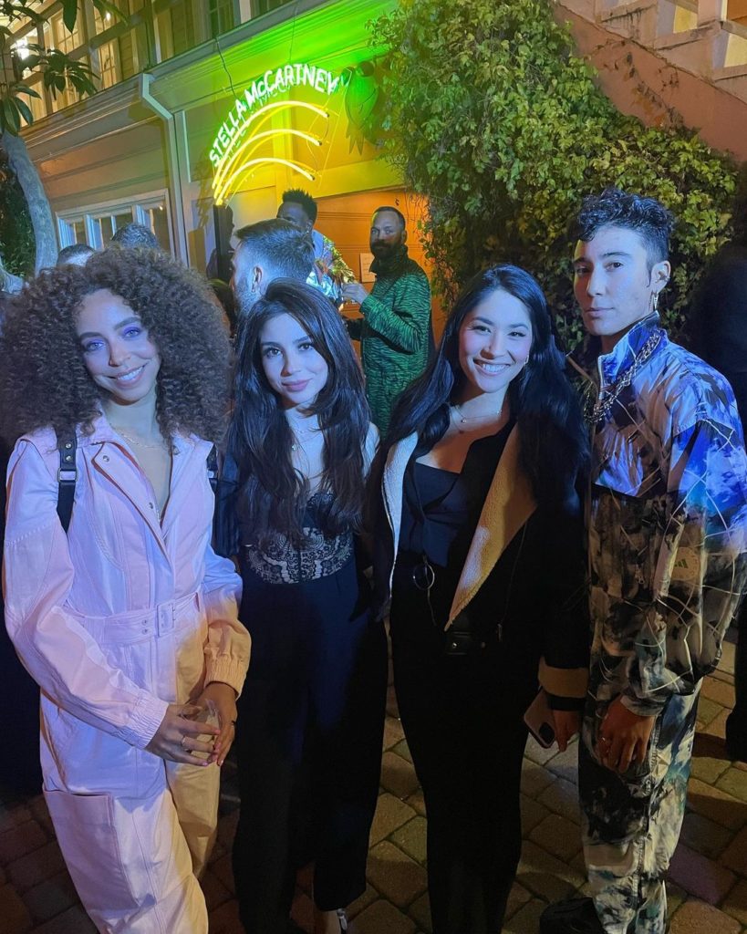 Vico stands with three other female-presenting people: Hayley Law, Sanam Sarani, and Natalie Handelsman. The neon “Stella McCartney” sign glows in the background.