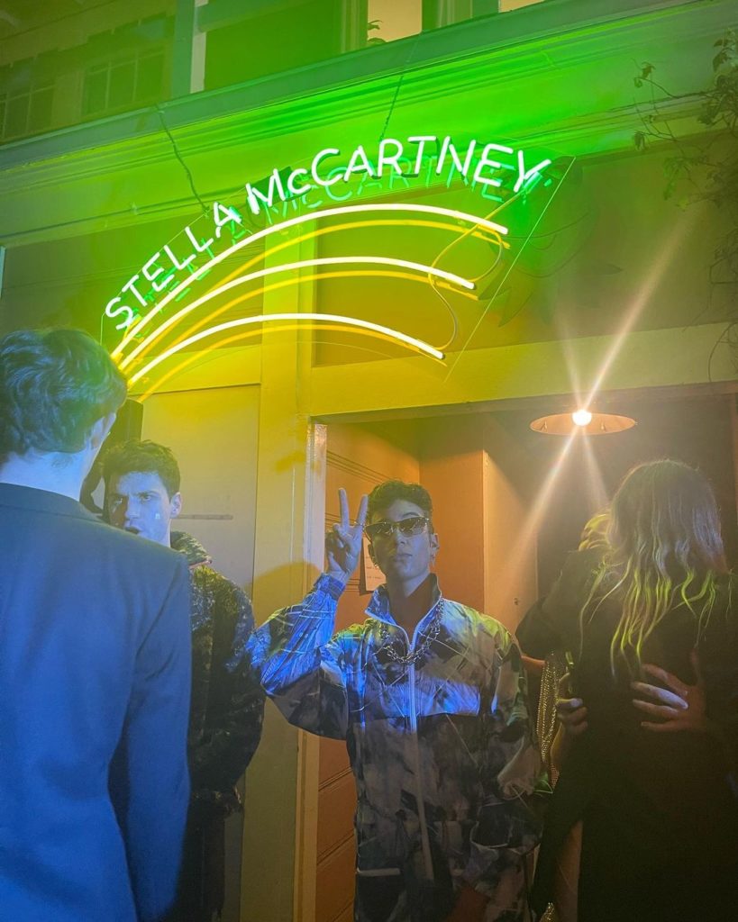 Vico makes a peace sign under the neon “Stella McCartney” sign.
