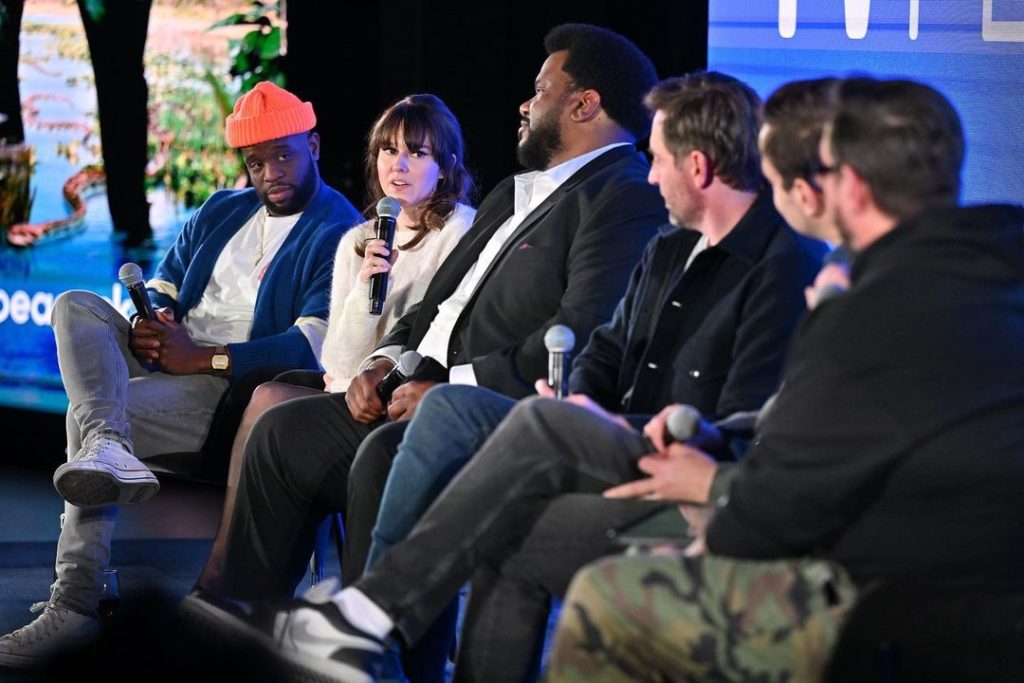 From SCAD TVFest 2023. Claudia has a mic in her hand, answering a question as part of a panel. Her "Killing It" stars are sitting in a line to her left and right.