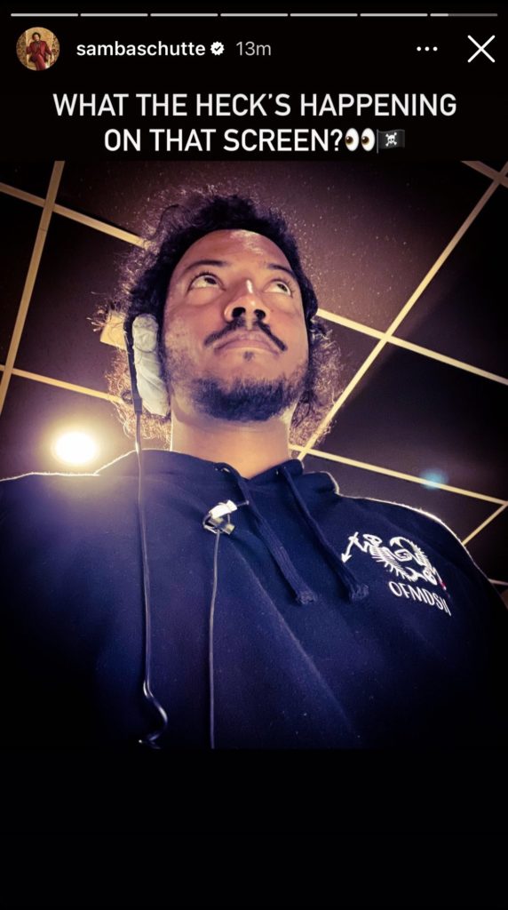 The camera is down very low, by Samba's hip, so you can only see him staring ahead at... something? He is wearing an OFMD S2 hoodie and a mic & headset. Text reads: "What the heck's happening on that screen? 👀🏴‍☠️"