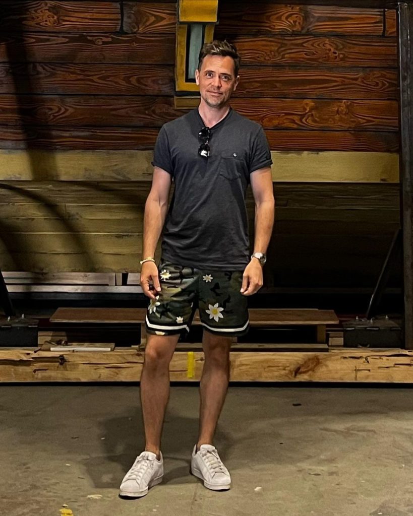 A full-body photo of David standing very close to the rear (whatever the nautical term is) of The Revenge. He is wearing a tshirt and shorts, very casual.