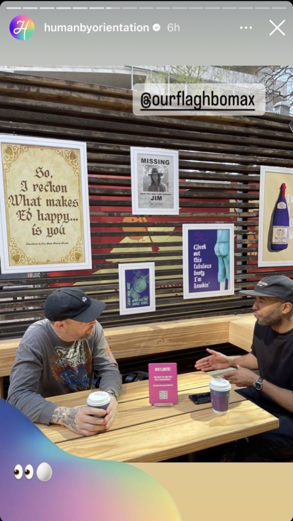 HBO's LGBTQ+ account Human by Orientation posts a story to Instagram. A man sits at a small table, talking to another man. Behind him are posters with OFMD quotes and art. HBO have added "👀🥚" to the picture.